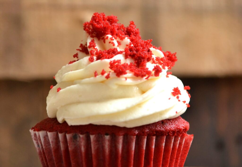 Picture of a red velvet cupcake with white frosting against a brown wooden background.