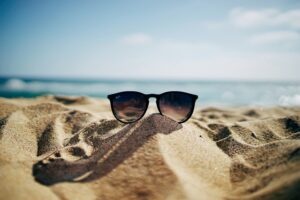 Sun glasses on a beach with the ocean behind them.