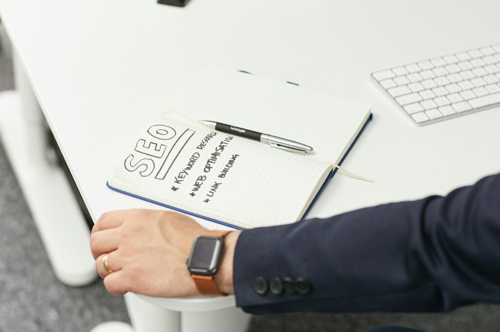 man's hand with a white notebook in frotn of him saying, SEO